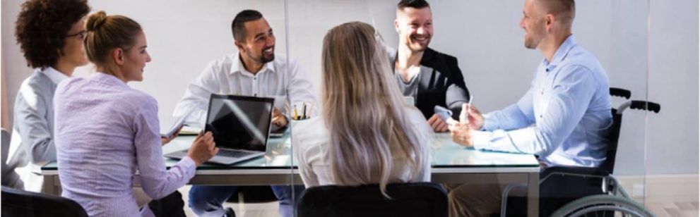 Group of coworkers with varying abilities meeting at boardroom table.