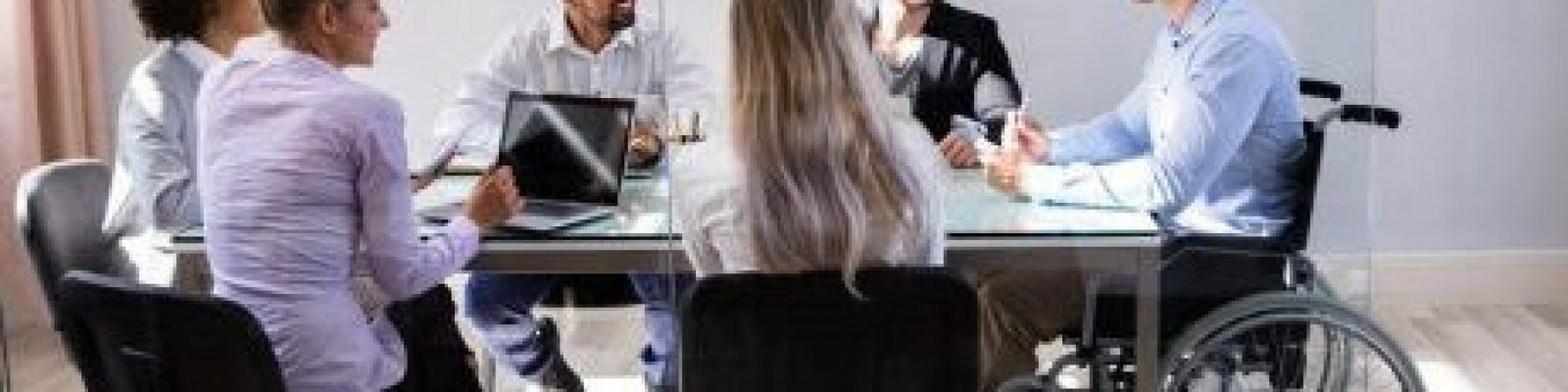 Group of coworkers with varying abilities meeting at boardroom table.